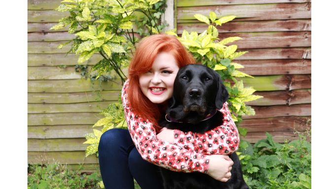 Lucy Edwards squatting in the grass with first guide dog Olga, a black lab